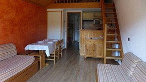 A cozy room with a dining table set for four, a wooden staircase, and a kitchen area with a microwave. - 2-room apartment, 4 people, Méribel center, close to shops & slopes (Méribel)