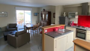 A modern kitchen with a central island, a dining area with a sofa and chairs, and a large window providing natural light. - At the gateway to the ocean (Penmarch)