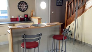 A kitchen with a wooden island, two bar stools, a clock, and a staircase. - At the gateway to the ocean (Penmarch)
