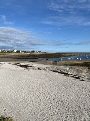 A sandy beach with boats in the water and houses in the background.