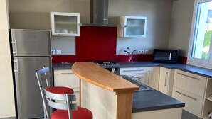 A modern kitchen with a central island, stainless steel appliances, and a red backsplash. - At the gateway to the ocean (Penmarch)