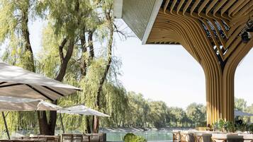An outdoor dining area with tables and chairs, surrounded by trees and a view of a body of water.