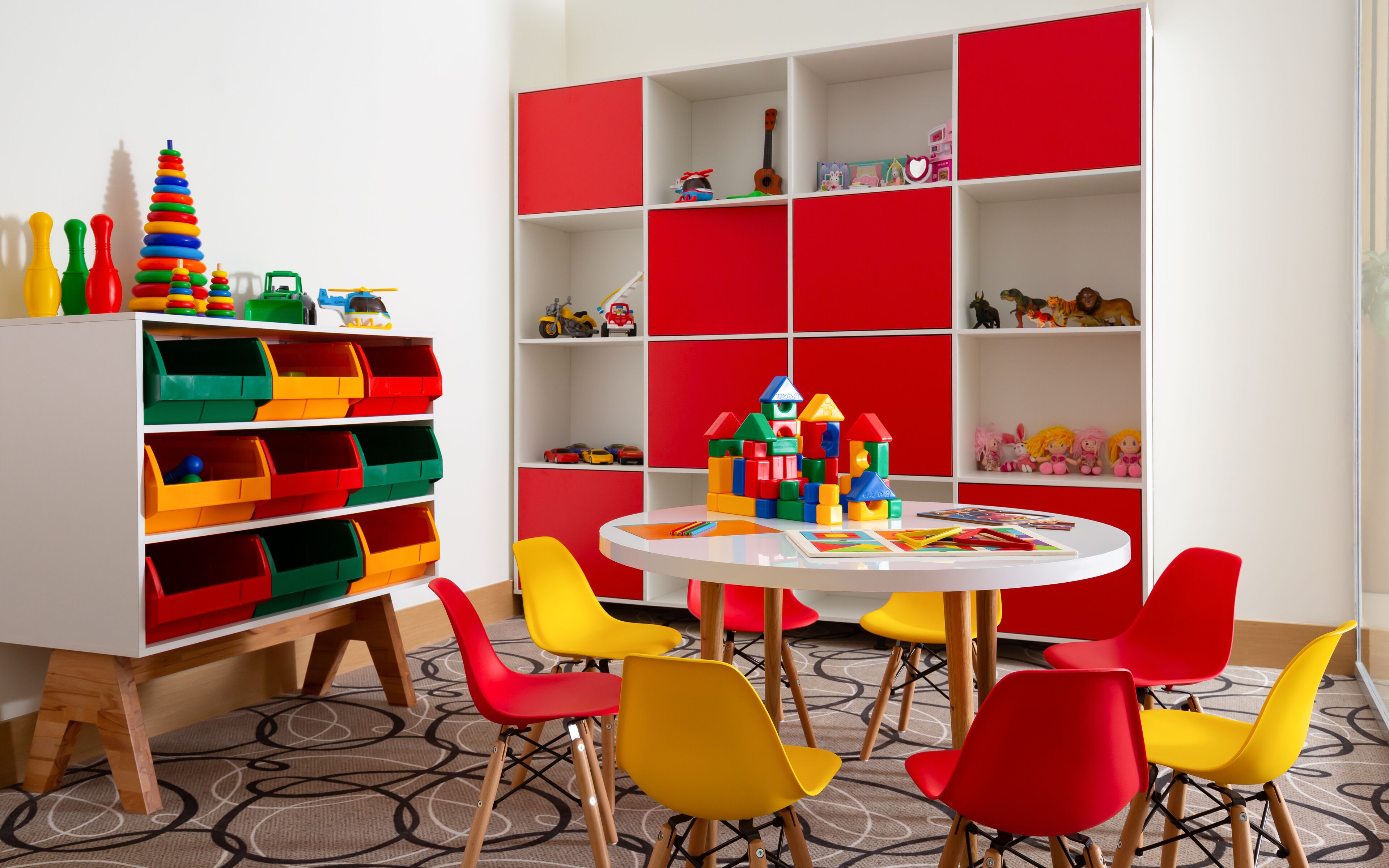 A children's playroom with colorful storage units, a play table, and bright chairs.