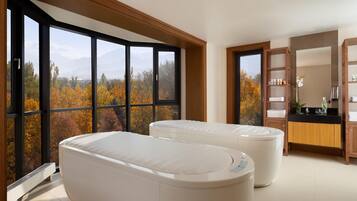 A modern bathroom with a large window, a bathtub, a shower area, and a vanity with toiletries.