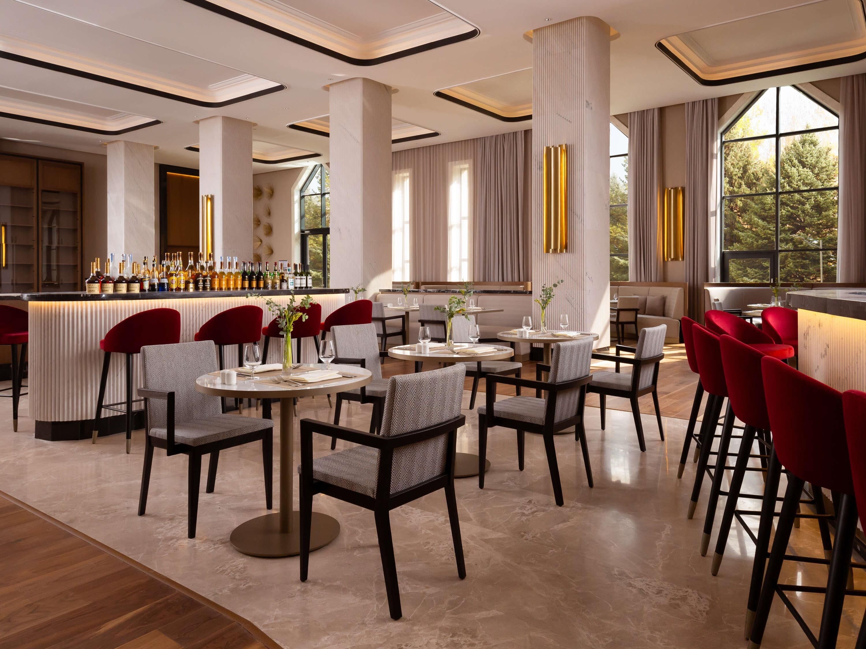 A modern restaurant with high ceilings, marble flooring, and a bar area with a variety of bottles.
