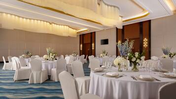 A banquet hall with round tables set for dining, white chairs, and floral centerpieces.