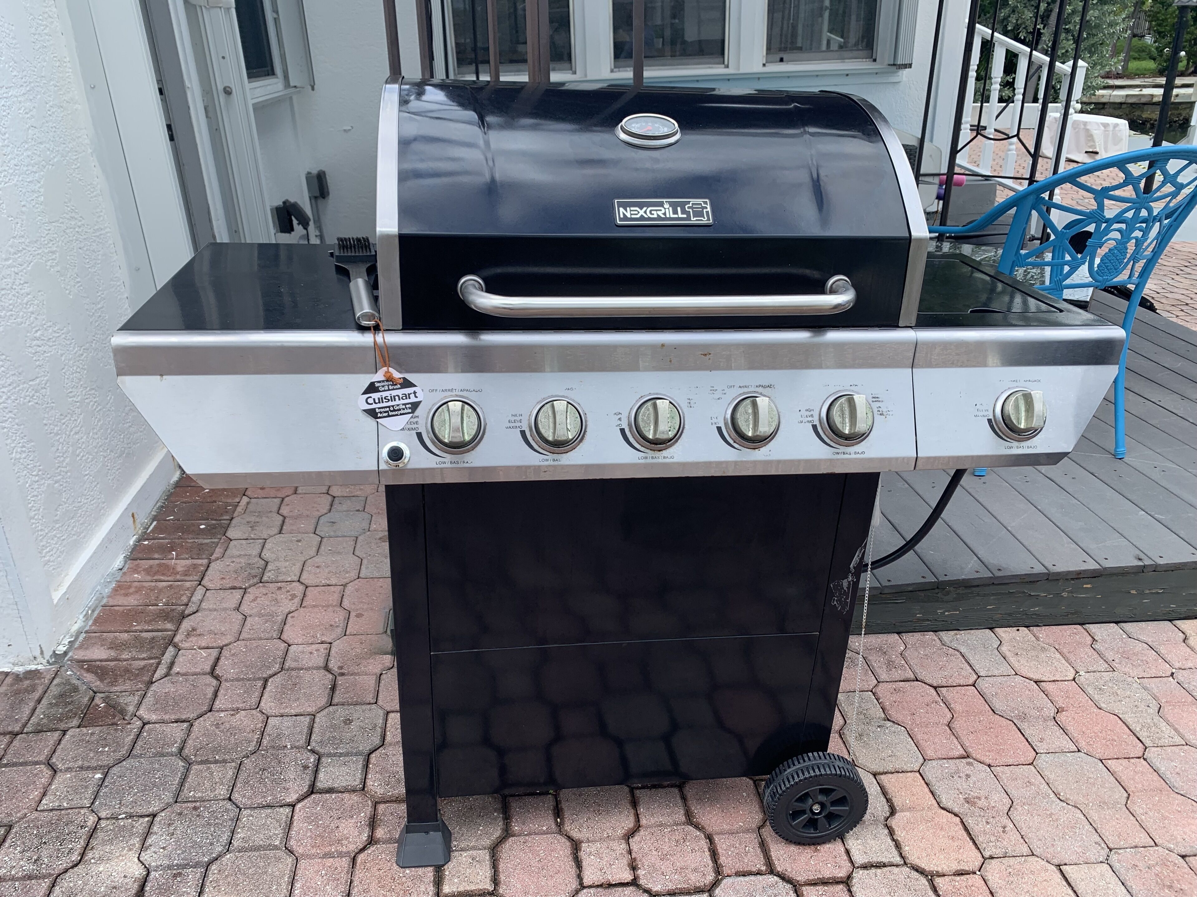 A NEXGRILL barbecue grill with four control knobs and a Cuisinart tag, placed on a brick patio.