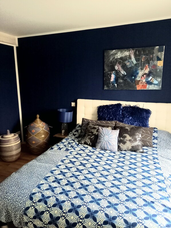 Une chambre avec un grand lit, des murs sombres et un tableau accroché au-dessus du lit.
