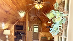 Een knus interieur van een chalet met houten plafond, een plafondventilator, een keukenhoek en een zithoek met een bank en vloerkleed.