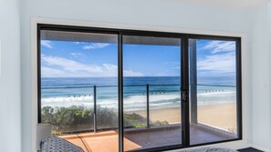 A room with a large sliding glass door leading to a balcony with a beach view.