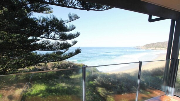 A balcony with a glass railing overlooking a beach and ocean.