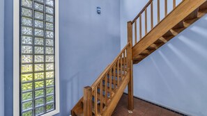 A wooden staircase with a handrail leading to a landing, adjacent to a window with a view of greenery.