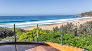 Vista da praia a partir de uma varanda com guarda-corpo, oceano e vegetação.
