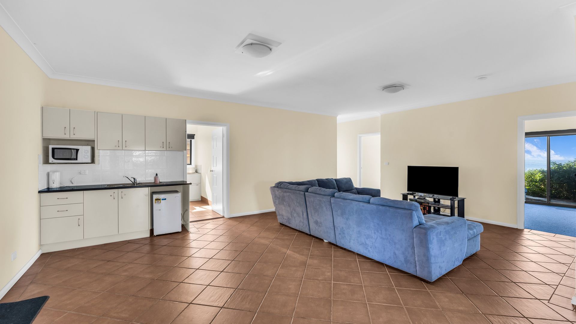 Un espacio habitable moderno con cocina, un sofá seccional azul y un televisor de pantalla plana.