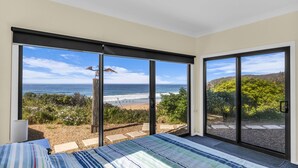 Quarto com uma grande porta de vidro deslizante que dá para uma varanda com vista para a praia.