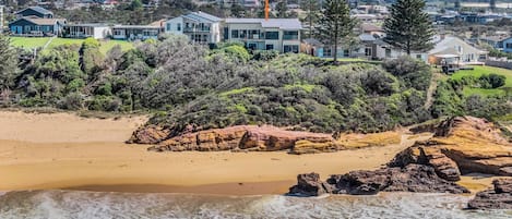 Une propriété située sur la côte, dotée d’une plage de sable, de formations rocheuses et bordée de maisons résidentielles.