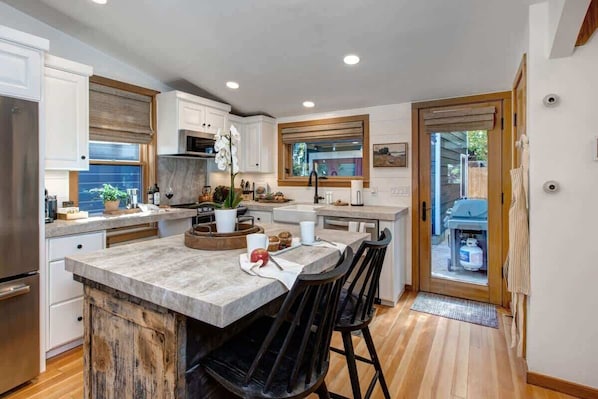 A modern kitchen with a central island, wooden flooring, and a view to the outside.