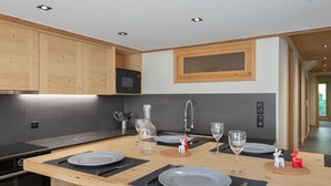 A modern kitchen with wooden cabinets, a built-in microwave, and a central island with a sink and seating area. - Family Apartment in Peaceful Area, Close to Slopes (Méribel)