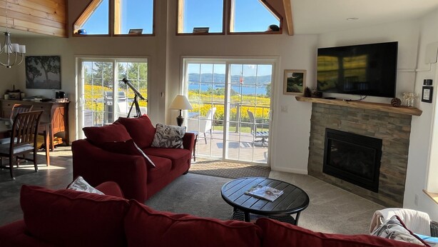 A spacious living room with a red sofa, a fireplace, a television, and a balcony with a scenic view.