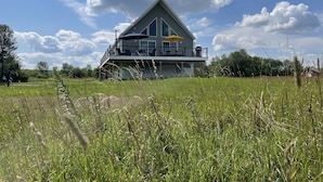 A two-story house with a balcony, surrounded by a grassy field.