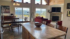 A spacious living area with a large wooden ceiling, a stone fireplace, and a dining area with a marble island.