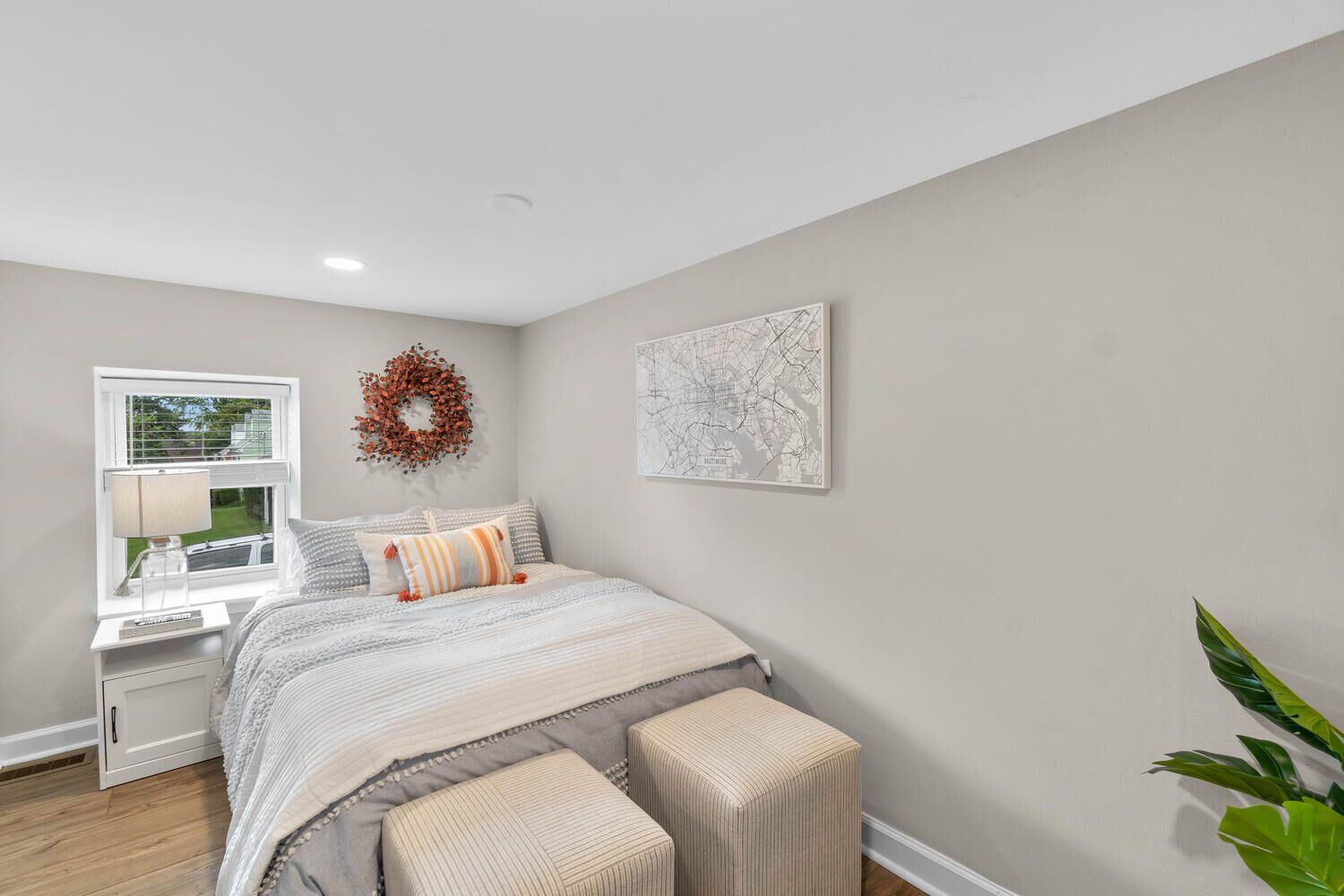 A bedroom with a bed, a window, a wall-mounted wreath, and a map.