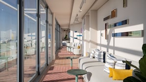 A modern hotel corridor with glass walls, a seating area with a sofa and cushions, and a tiled floor. - Home Suite Hotels Sea Point (Cape Town)