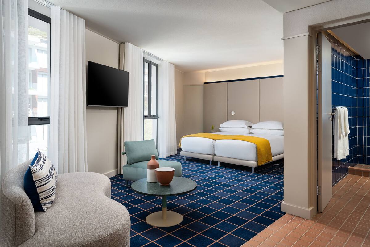 Et hotelværelse med seng, sofa, fjernsyn og badeværelse med blå fliser.