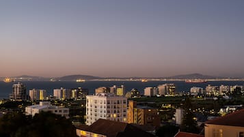 A coastal cityscape at dusk with high-rise buildings and a view of the sea.