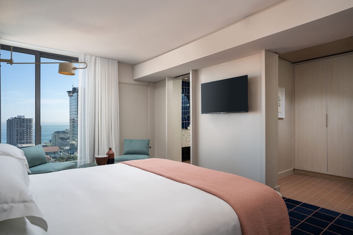 Et hotelværelse med en stor seng, et fjernsyn ophængt på væggen og udsigt over bybilledet samt en silhuet af byens skyline gennem vinduet.