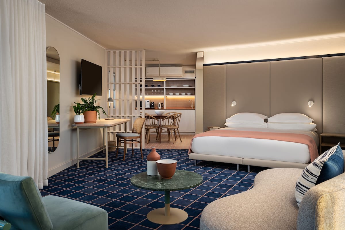 Et lille hotelværelse med seng, spiseplads, fjernsyn og tekøkken.