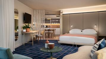 A compact hotel room with a bed, a small dining area, a TV, and a kitchenette.