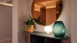 A hallway with a round mirror, a potted plant, a lit table lamp, and a decorative vase. - Home Suite Hotels Sea Point (Cape Town)