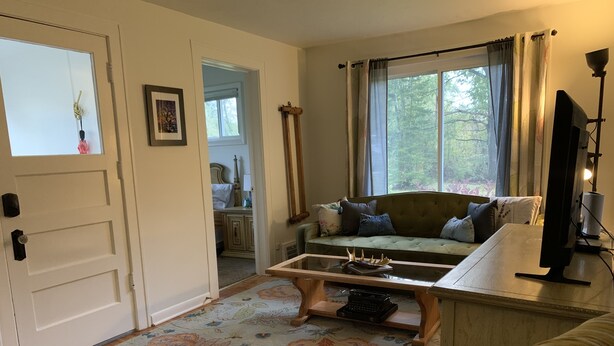A cozy living room with a sofa, a coffee table, and a television. There is a door leading to another room and a window with curtains.