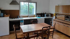 Cocina compacta con estufa a gas, microondas y horno, una ventana con vistas a zonas verdes, y un comedor con mesa y sillas de madera.