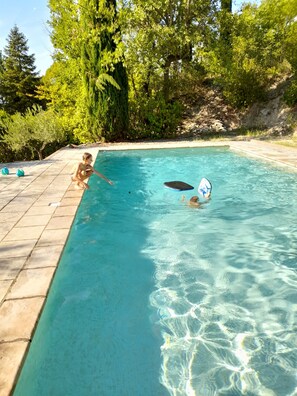 A clear swimming pool with tiled edges, surrounded by trees and a stone wall.