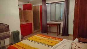 Un dormitorio con cama, una mesita, un radiador, una ventana con cortinas y un armario.