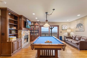 A pool table in a room with wooden cabinets, a fireplace, and a bookshelf.