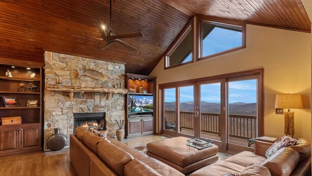 A spacious living room with a stone fireplace, leather sofas, wooden shelves, and a large window with a mountain view. - Breathtaking 2-Level Mountain Retreat (Blowing Rock)