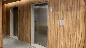Käytävä, jossa on kaksi hissiä, seinät on verhoiltu puupaneloinnilla ja lattia on laatoitettu.