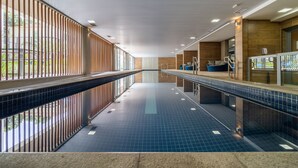 Una piscina interior moderna, de diseño largo y estrecho, con paredes alicatadas y una vista despejada del exterior a través de amplias ventanas.