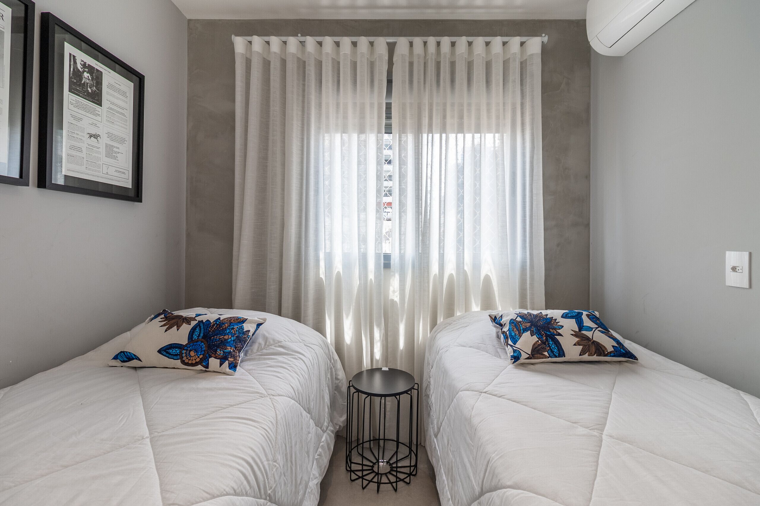 A bedroom with two beds, a small round table, and a window with sheer curtains.