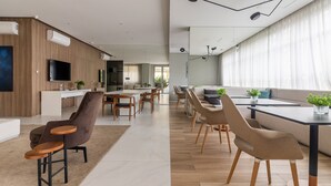 Una sala de estar moderna con un sofá, sillones y una mesa de centro. Cuenta con un comedor con mesa y sillas. La habitación tiene un ventanal con cortinas.