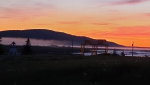 Un coucher de soleil sur un paysage comprenant un belvédère, un petit bâtiment et un pont.
