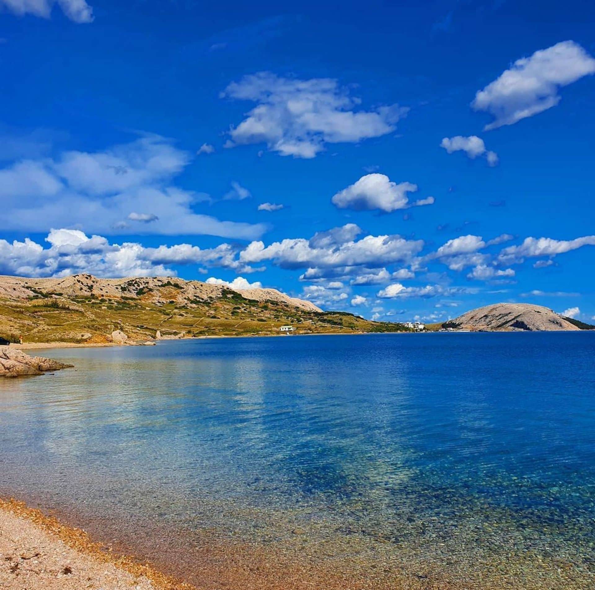 Mar azul cristalina con costa rocosa y montañas al fondo bajo un cielo despejado.