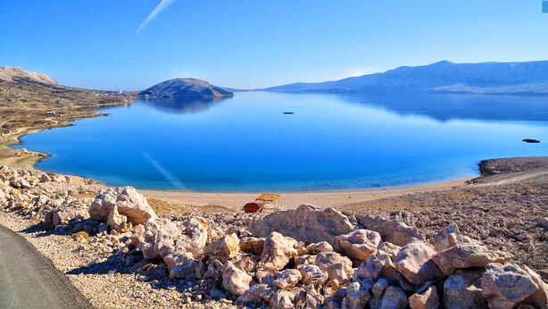 A clear view of a large, calm lake with a rocky shoreline and a distant mountain range. - 2 Bed Flat - Sleeps 8 - Parking - Wifi (Novalja)