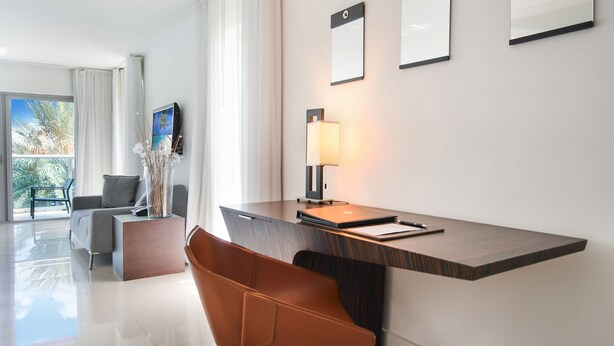 Moderni hotellihuone, jossa on suuri ikkuna, työpöytä lampun kanssa, tuoli ja sohva.