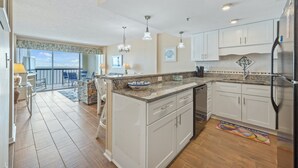 Una cocina amplia con gabinetes blancos, encimera de granito y refrigerador de acero inoxidable.
