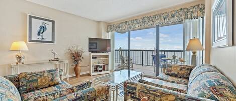 A spacious living room with a balcony, a television, and a dining area.