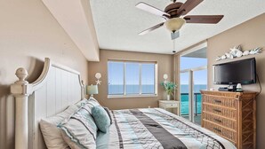 A bedroom with a bed, a ceiling fan, a TV, and a view of the ocean. - Luxurious Oceanfront Penthouse with Private Glass-Walled Balcony | Crescent Keyes - PH 9 (North Myrtle Beach)